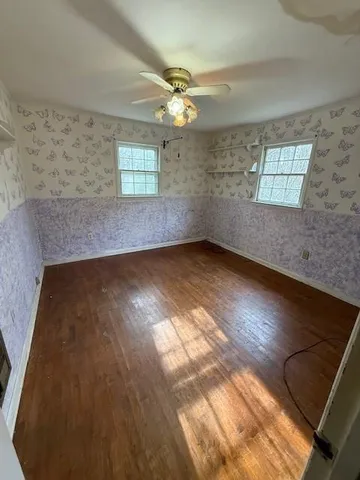 an empty room with wooden floor fan and windows