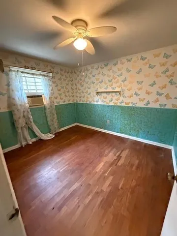 an empty room with wooden floor fan and a window
