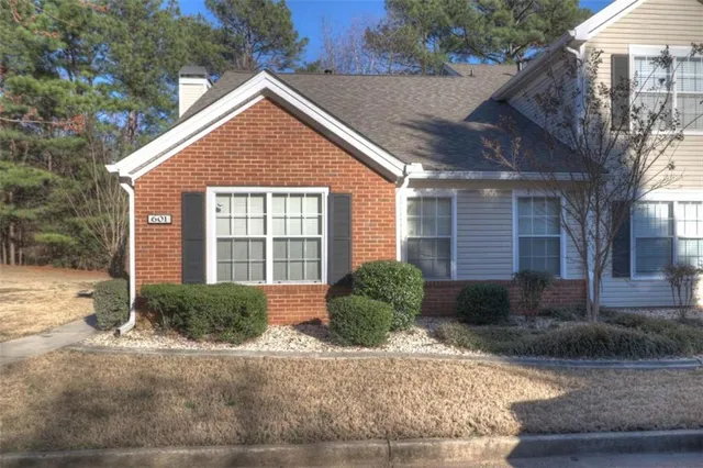 a view of a brick house with a yard plants and large tree