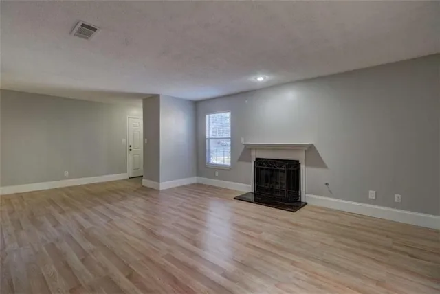 an empty room with wooden floor fireplace and windows