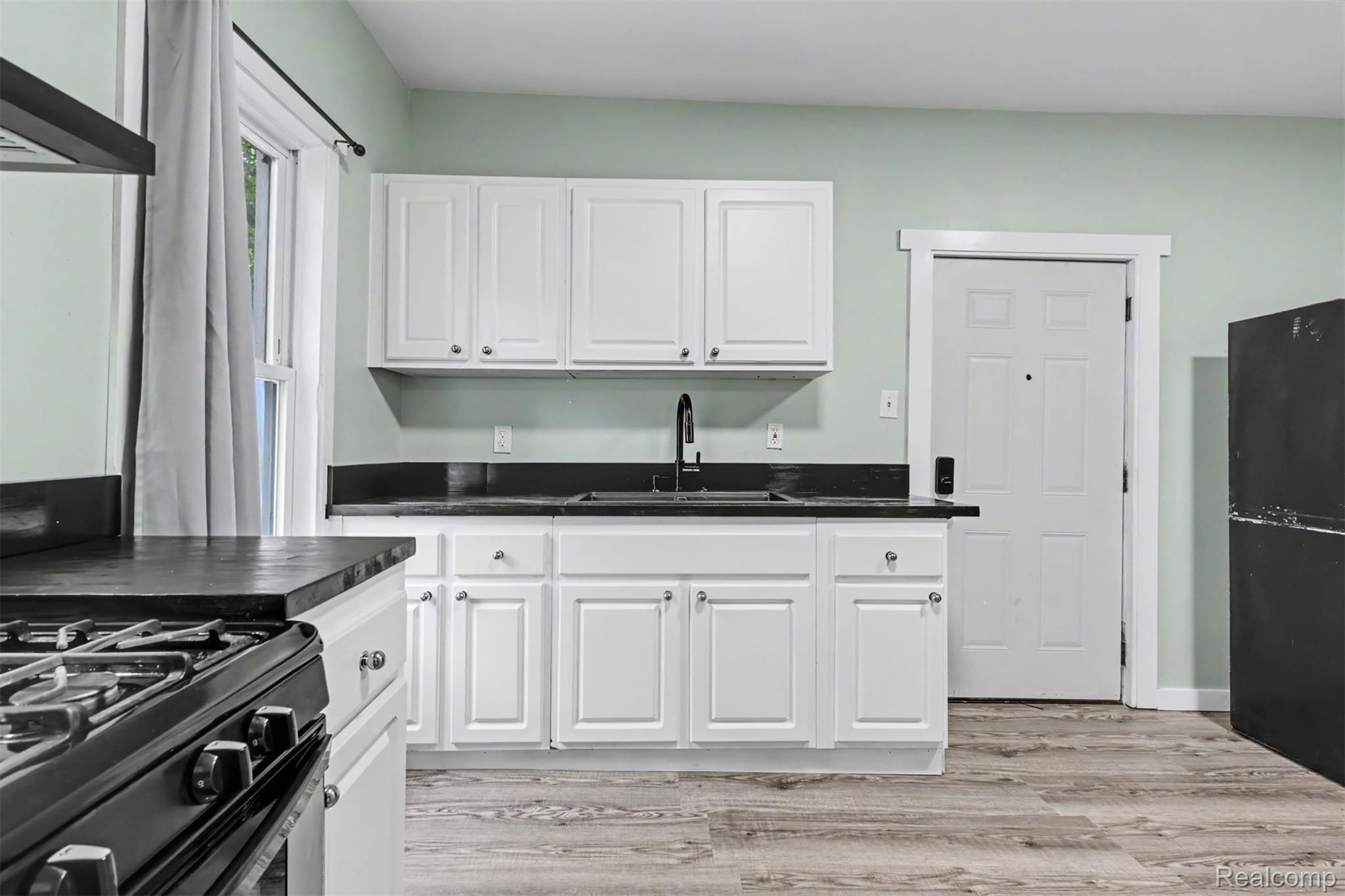 8397 Lane Street Detroit, MI 48209 - Photo 12 of 41 Kitchen featuring white cabinetry, dark countertops, a black sink with a matte black faucet, and wood-finish flooring