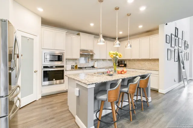 a kitchen with stainless steel appliances kitchen island granite countertop a stove top oven a refrigerator a sink and a dining table with wooden floor