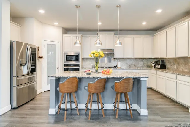 a kitchen with stainless steel appliances granite countertop a refrigerator a stove top oven a sink dishwasher and white cabinets with wooden floor