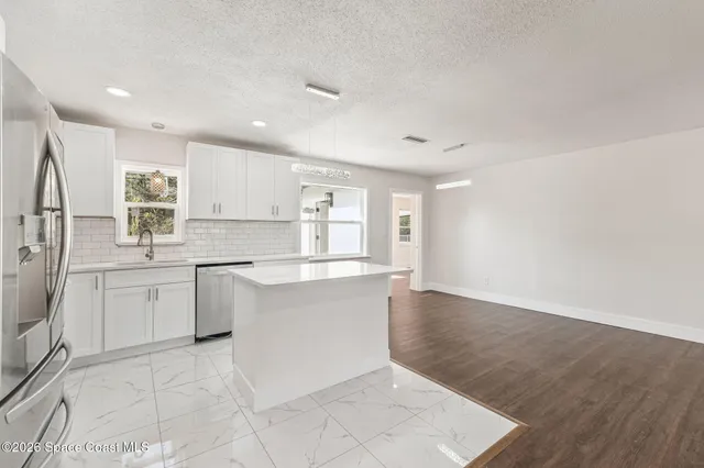 a large white kitchen with a sink a refrigerator and white cabinets