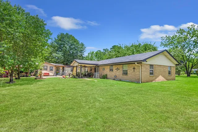 a view of a house with a big yard and potted plants and large trees
