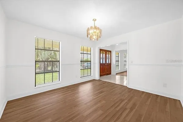 an empty room with wooden floor chandelier and windows