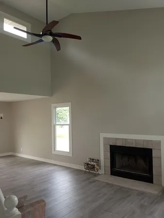 a view of an empty room with wooden floor fireplace and a window