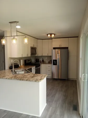 a kitchen with stainless steel appliances granite countertop a refrigerator a stove a sink and white cabinets with wooden floor