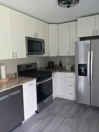 a kitchen with stainless steel appliances granite countertop a refrigerator stove a sink and white cabinets