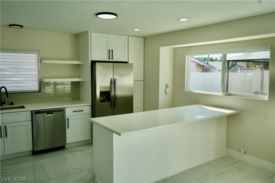 2351 Valleywood Road Henderson, NV 89014 - Photo 11 of 43 Kitchen featuring light marble finish flooring, white cabinetry, stainless steel appliances, a peninsula, and tasteful backsplash