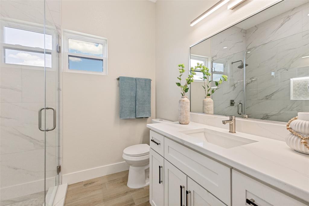3150 Crisp Road Ennis, TX 75119 - Photo 19 of 30 Contemporary bathroom featuring a spacious glass-enclosed shower, dual windows, a floating vanity with a single basin, a large wall-mounted mirror, and wood-finish flooring