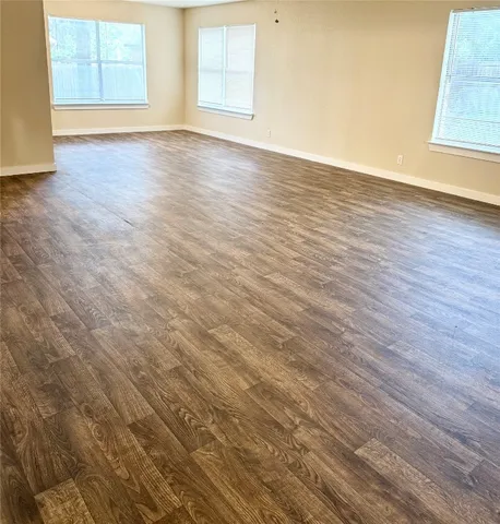 a view of an empty room with wooden floor and windows