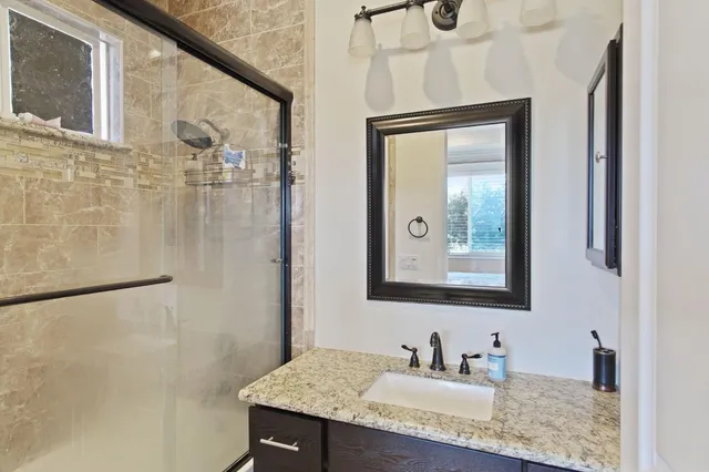 a bathroom with a granite countertop sink a mirror and shower