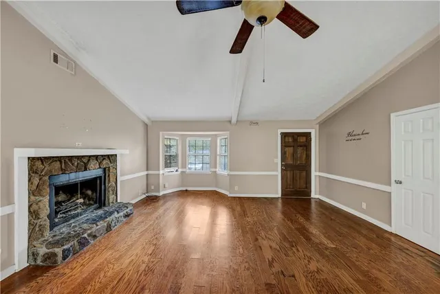 an empty room with wooden floor fireplace cabinet and windows