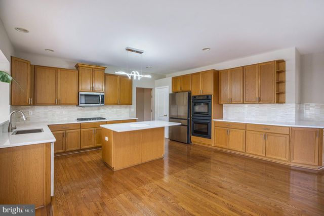 a large kitchen with stainless steel appliances granite countertop a stove a sink a refrigerator white cabinets and wooden floor