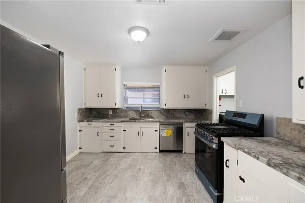 a kitchen with granite countertop a sink a stove a refrigerator and white cabinets