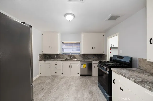 a kitchen with granite countertop a sink a stove a refrigerator and white cabinets