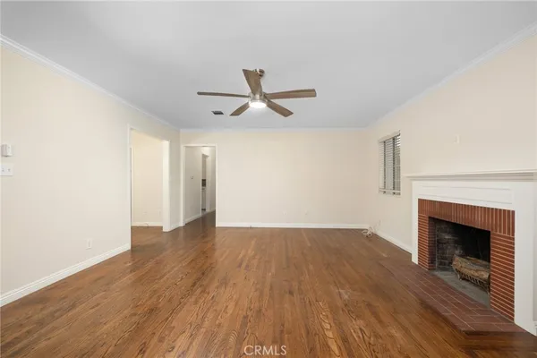 an empty room with wooden floor a ceiling fan a fireplace and windows