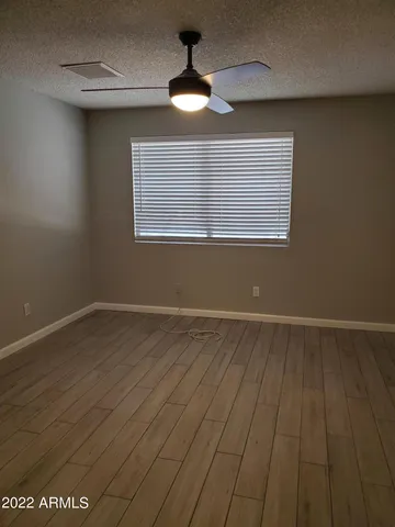 an empty room with wooden floor chandelier fan and windows