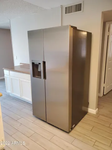 a view of a refrigerator in kitchen and an empty room in wooden floor