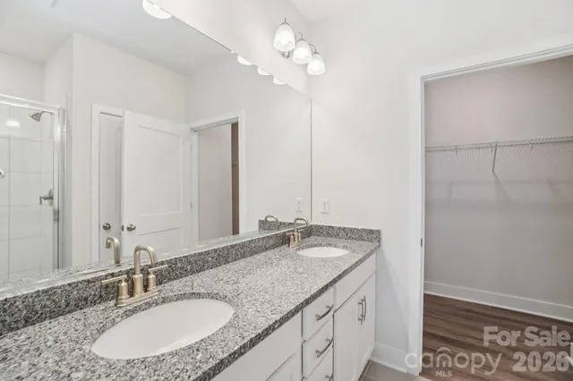 a bathroom with a granite countertop double vanity sink a mirror and a shower