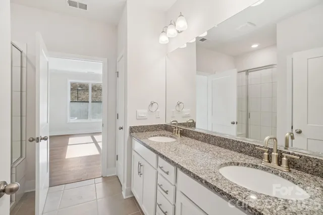 a bathroom with a granite countertop double vanity sink a mirror and shower