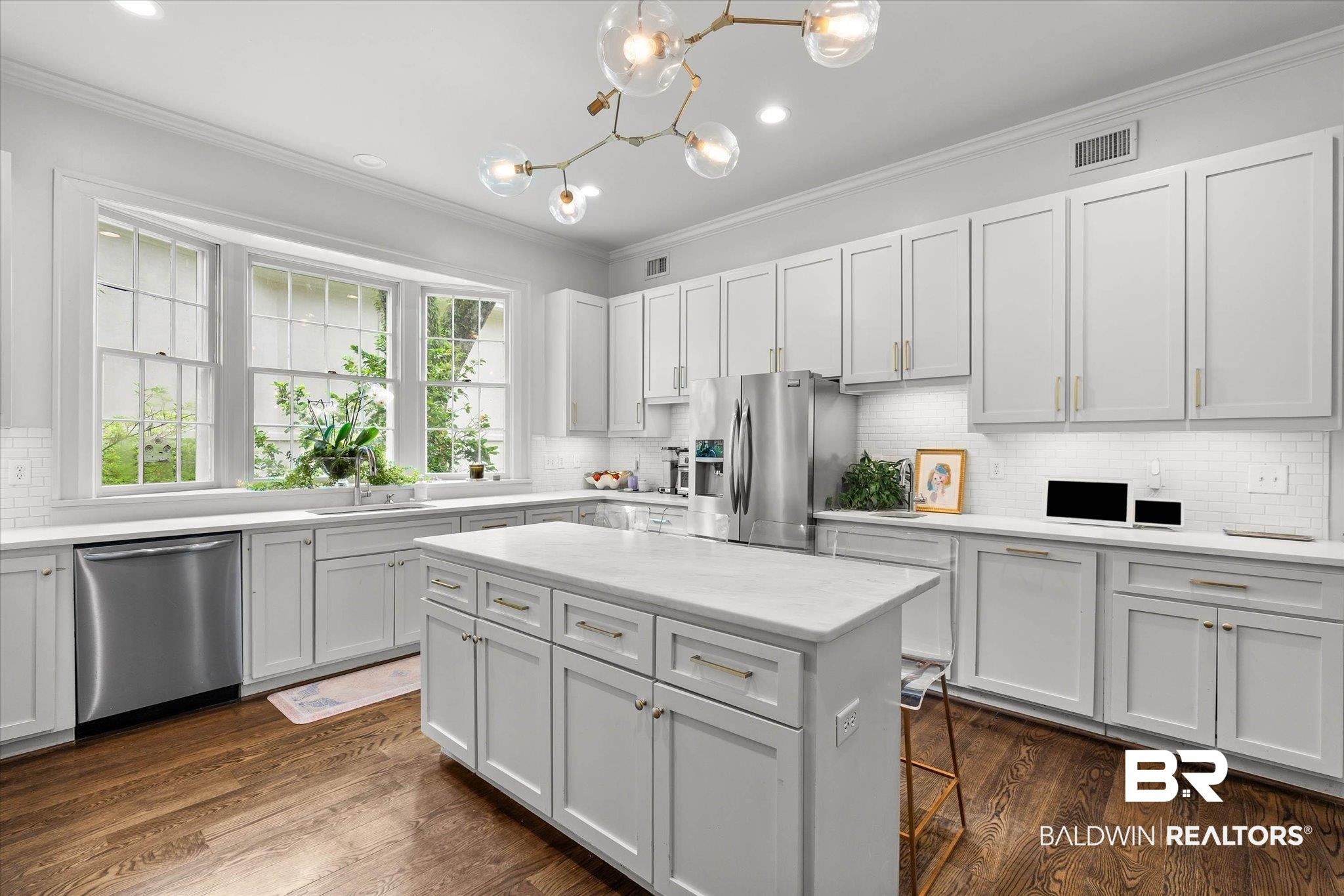 3908 Yester Place Mobile, AL 36608 - Photo 15 of 45 Modern kitchen featuring white shaker-style cabinetry, a central island with a light-toned countertop, stainless steel appliances, and wood-finish flooring