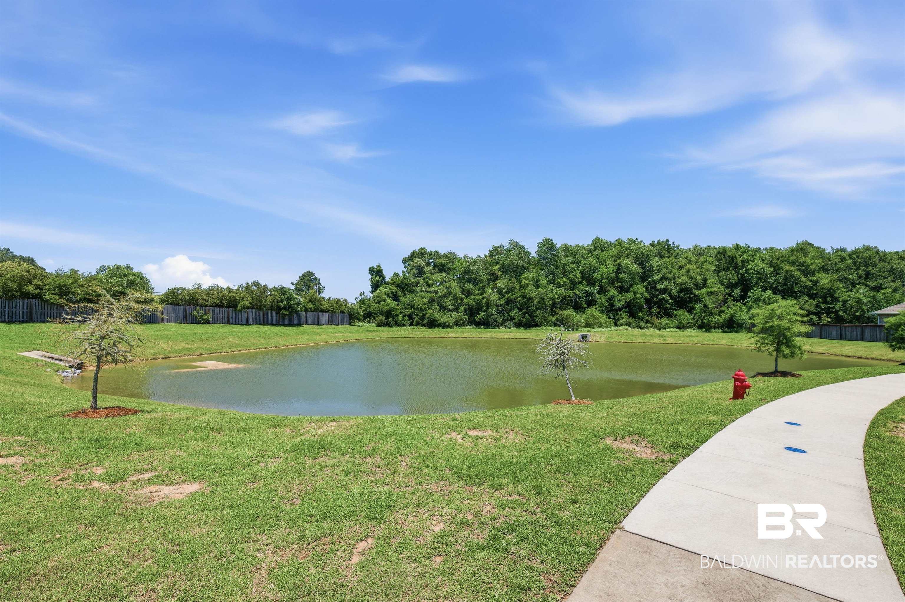 8735 Bronze Lane Foley, AL 36535 - Photo 52 of 58 Expansive green space featuring a tranquil pond, manicured lawn, and mature tree line