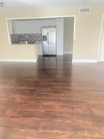 a view of an empty room and kitchen with wooden floor
