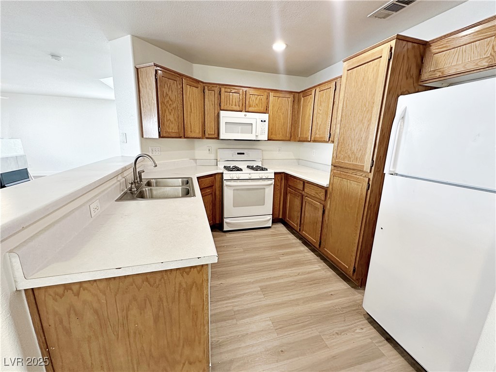 9416 Moon Splash Court Las Vegas, NV 89129 - Photo 16 of 47 Kitchen with white appliances, light countertops, light wood-style floors, brown cabinetry, and a peninsula
