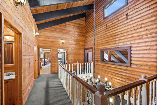 4725 Pine Ridge Road Evanston, UT 82930 - Photo 25 of 82 Upper-level hallway featuring extensive wood paneling, exposed wood beams, vaulted ceilings, and a light-colored wood railing
