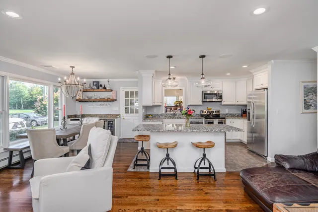 a living room with stainless steel appliances kitchen island granite countertop a dining table chairs and a refrigerator