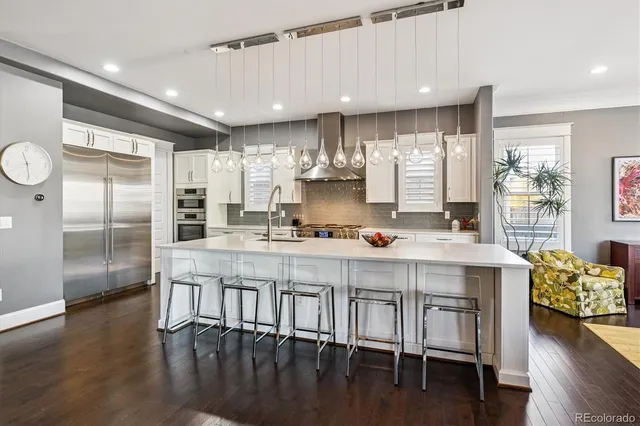 a kitchen with stainless steel appliances granite countertop a stove top oven a sink a refrigerator and white cabinets with wooden floor