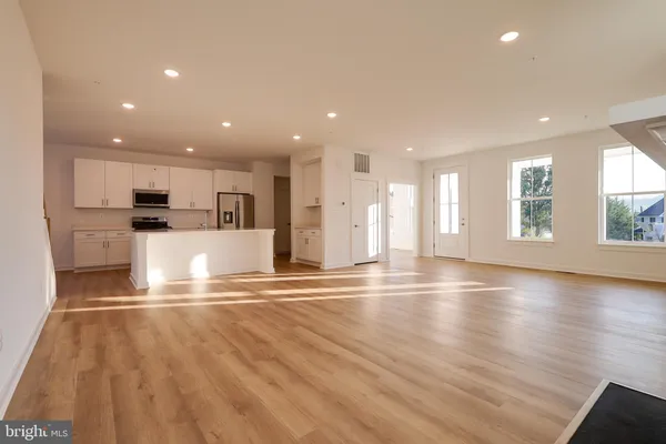 an empty room with kitchen view and living room with wooden floor