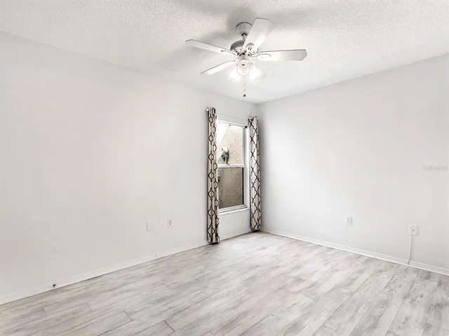an empty room with wooden floor chandelier fan and windows