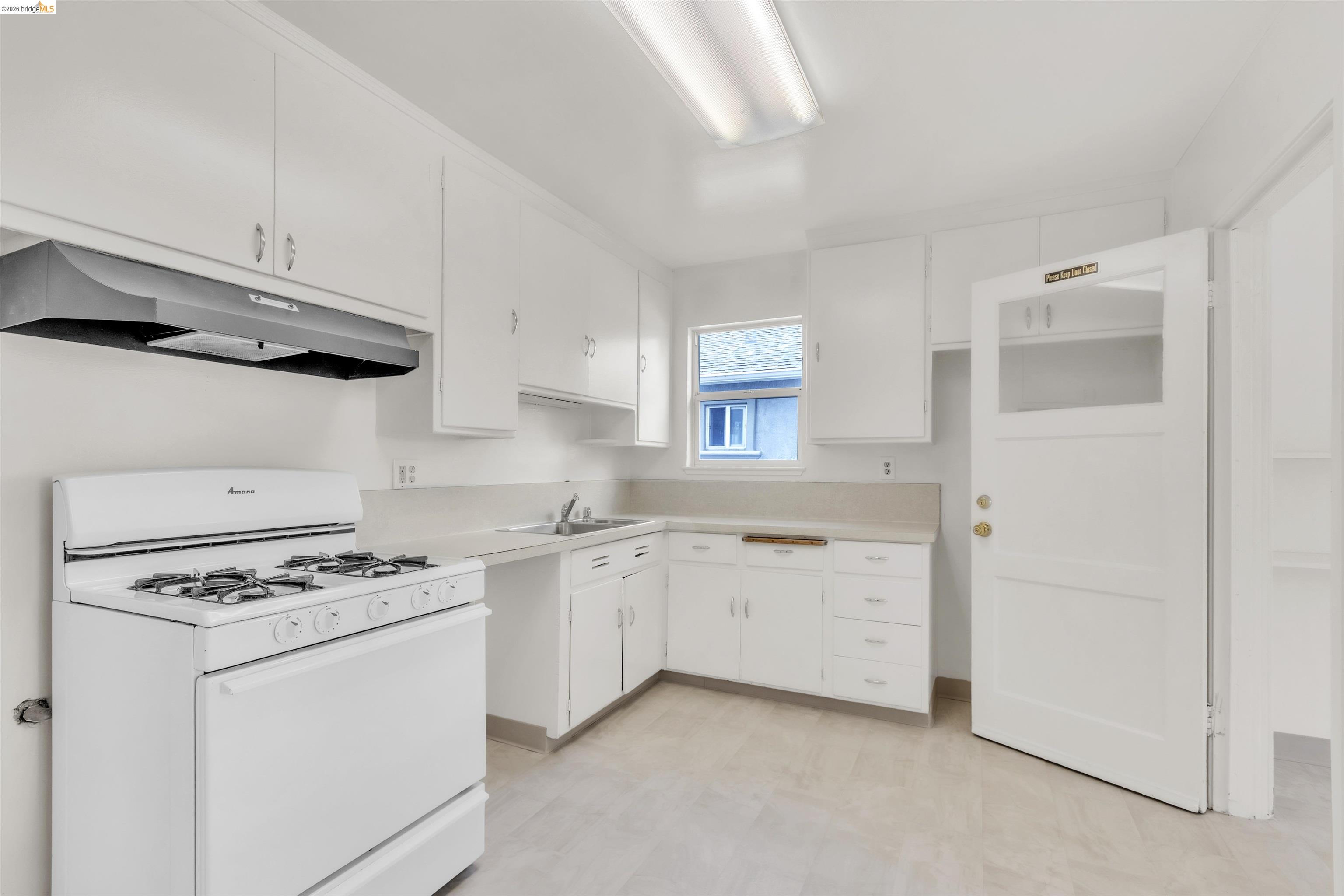 621 Paseo Del Rio San Lorenzo, CA 94580 - Photo 7 of 24 Kitchen featuring a white gas range with overhead ventilation, extensive white cabinetry, light-toned countertops, and a single window