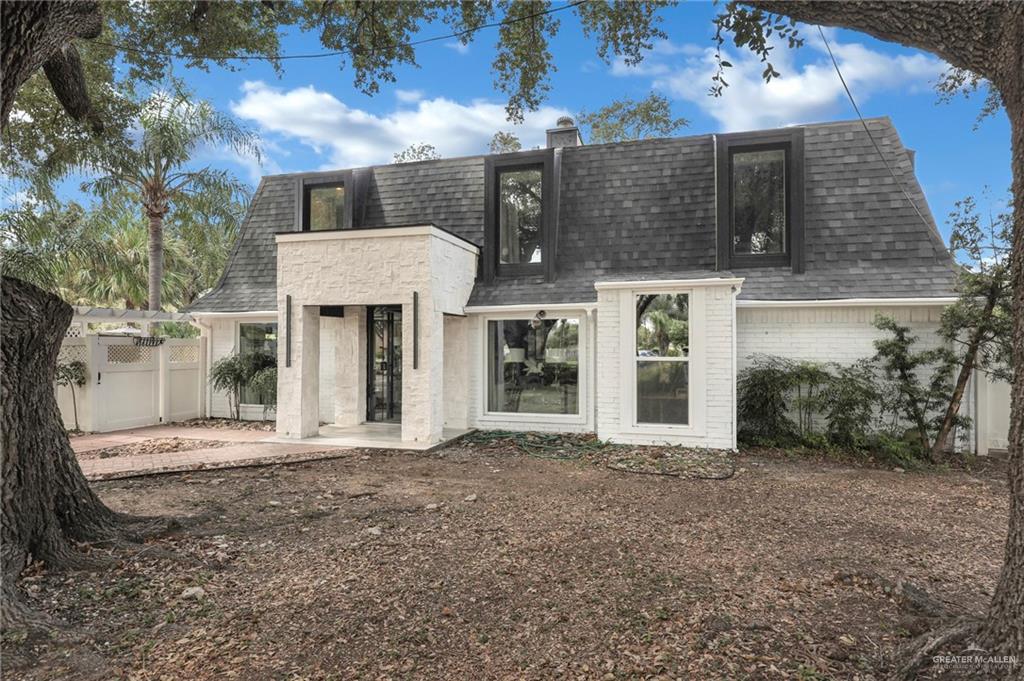 Back of property with a shingled roof, mansard roof, brick siding, and a chimney