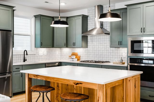 a large kitchen with granite countertop a stove a sink dishwasher a refrigerator and a dining table with wooden floor