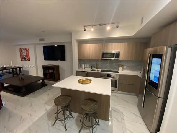 a kitchen with stainless steel appliances kitchen island granite countertop a sink a stove a microwave a refrigerator a counter top and chairs