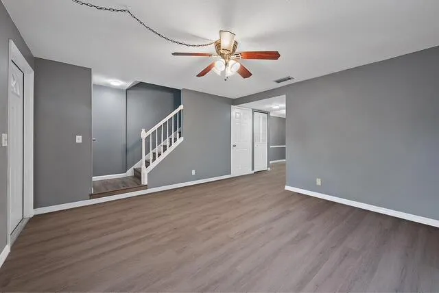 a view of an empty room with wooden floor and a ceiling fan