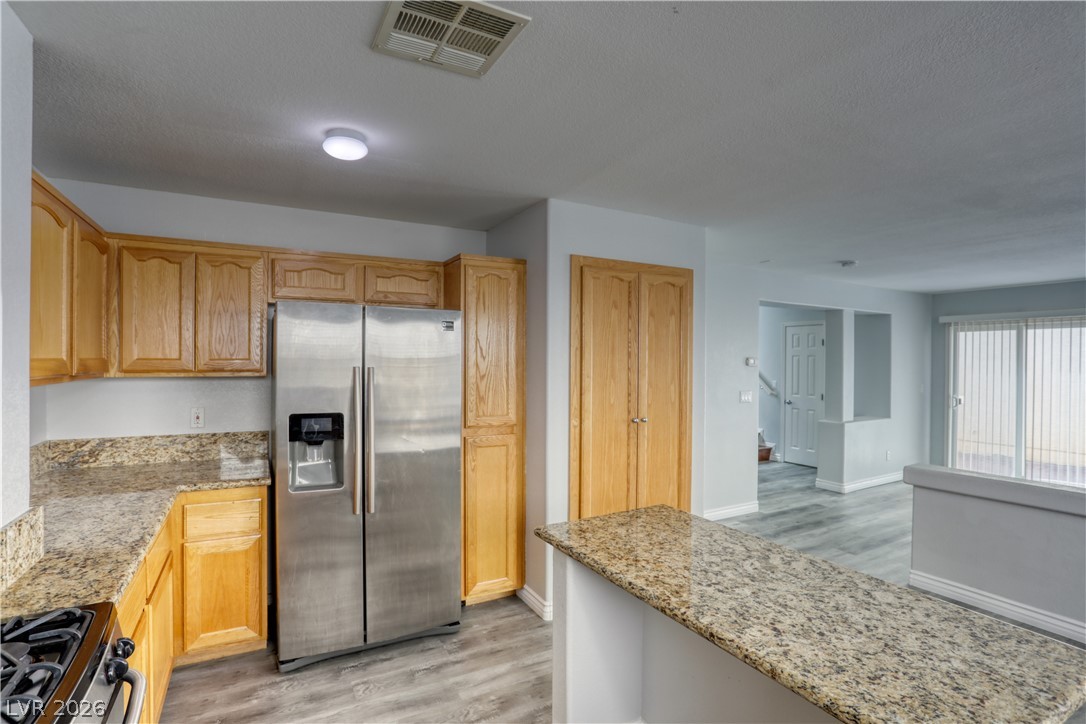 7226 Cestrum Road Las Vegas, NV 89113 - Photo 4 of 28 Kitchen with stainless steel fridge, light wood finished floors, range with gas cooktop, light stone counters, and a textured ceiling