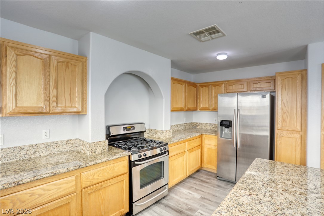 7226 Cestrum Road Las Vegas, NV 89113 - Photo 5 of 28 Kitchen featuring stainless steel appliances, light stone countertops, light wood finish cabinetry, and light wood finished floors