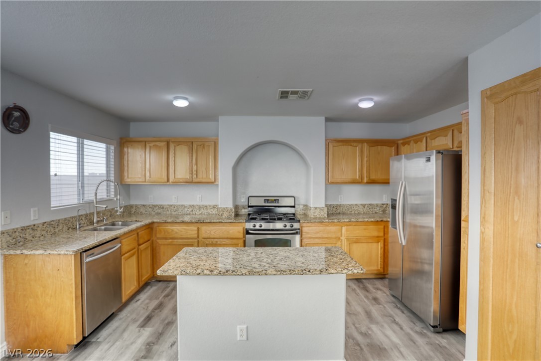 7226 Cestrum Road Las Vegas, NV 89113 - Photo 6 of 28 Kitchen with stainless steel appliances, light stone countertops, light wood-style flooring, and a kitchen island