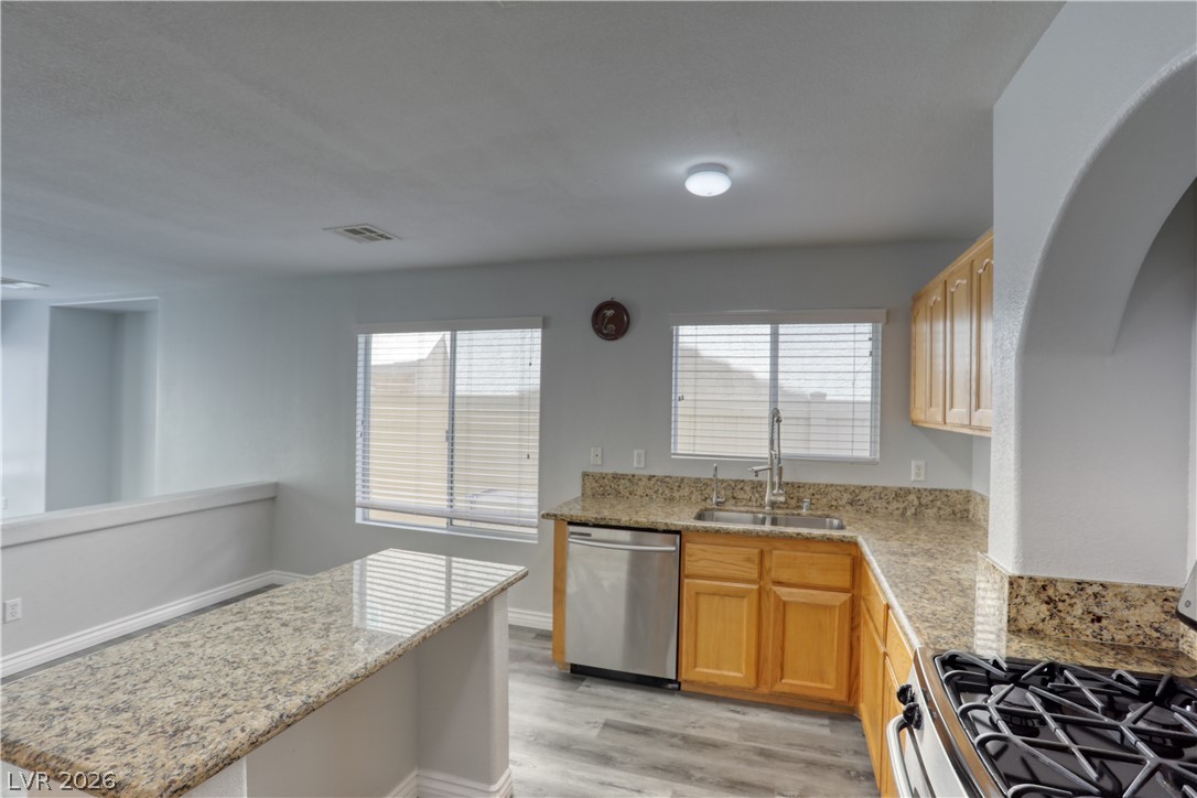 7226 Cestrum Road Las Vegas, NV 89113 - Photo 8 of 28 Kitchen featuring stainless steel appliances, healthy amount of natural light, light stone counters, and light wood finished floors