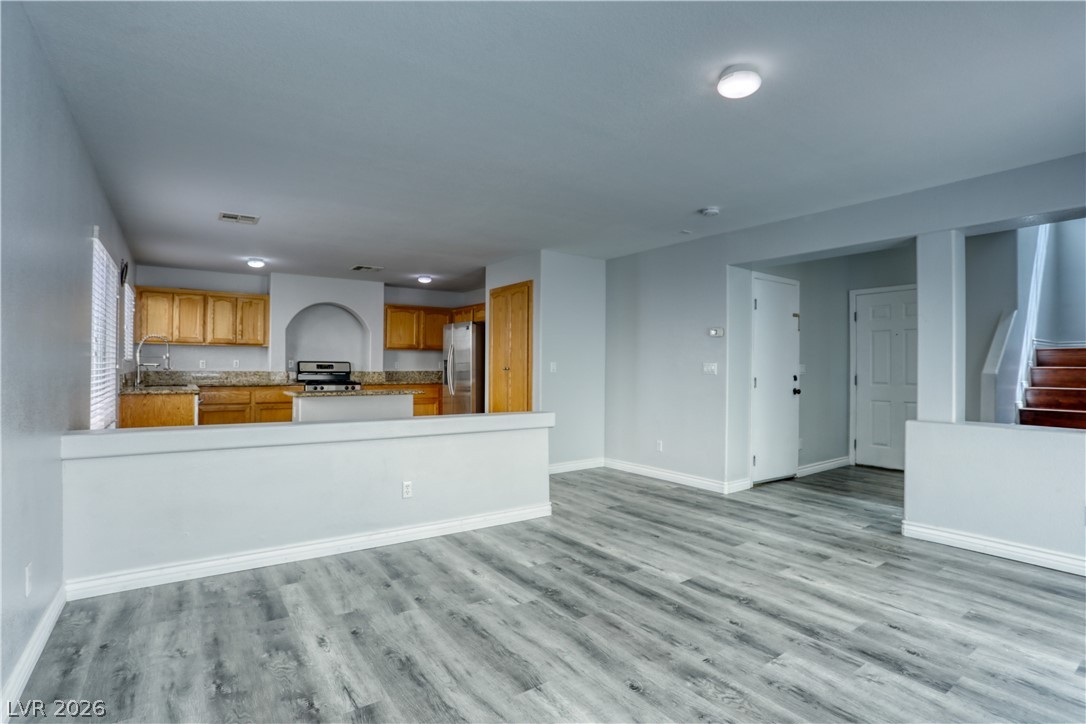 7226 Cestrum Road Las Vegas, NV 89113 - Photo 28 of 28 Kitchen featuring open floor plan, stainless steel appliances, wood finish cabinets, light wood finished floors, and light stone counters