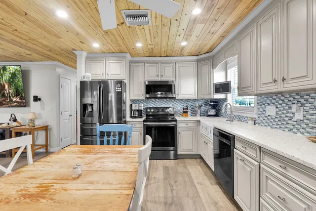a kitchen with stainless steel appliances granite countertop a stove top oven a sink dishwasher a refrigerator and a dining table with wooden floor