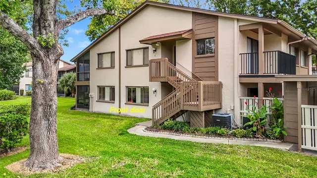 a view of a white house with a big yard and potted plants and large trees