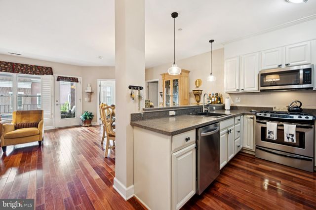 a kitchen with stainless steel appliances granite countertop a stove a sink dishwasher a refrigerator white cabinets wooden floor and a view of living room