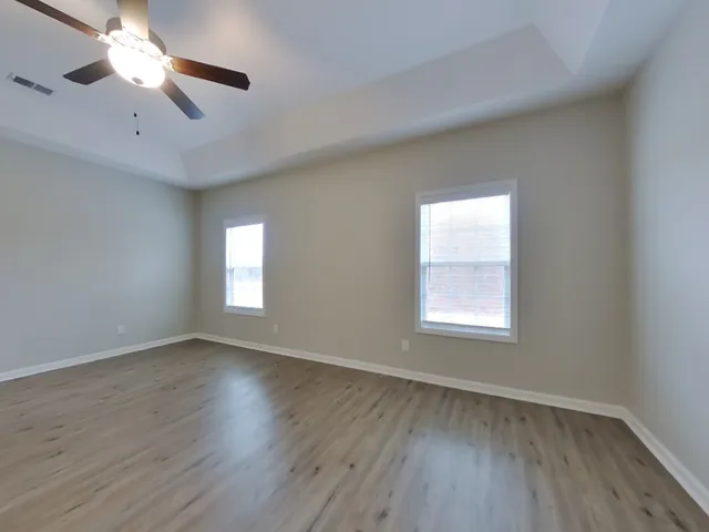 an empty room with wooden floor chandelier fan and windows