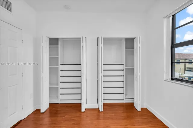 an empty room with wooden floor closet and windows
